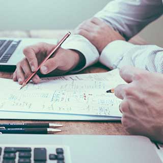 Photo of two 
                    people working together at a desk representative of MSI working with the client to plan security.